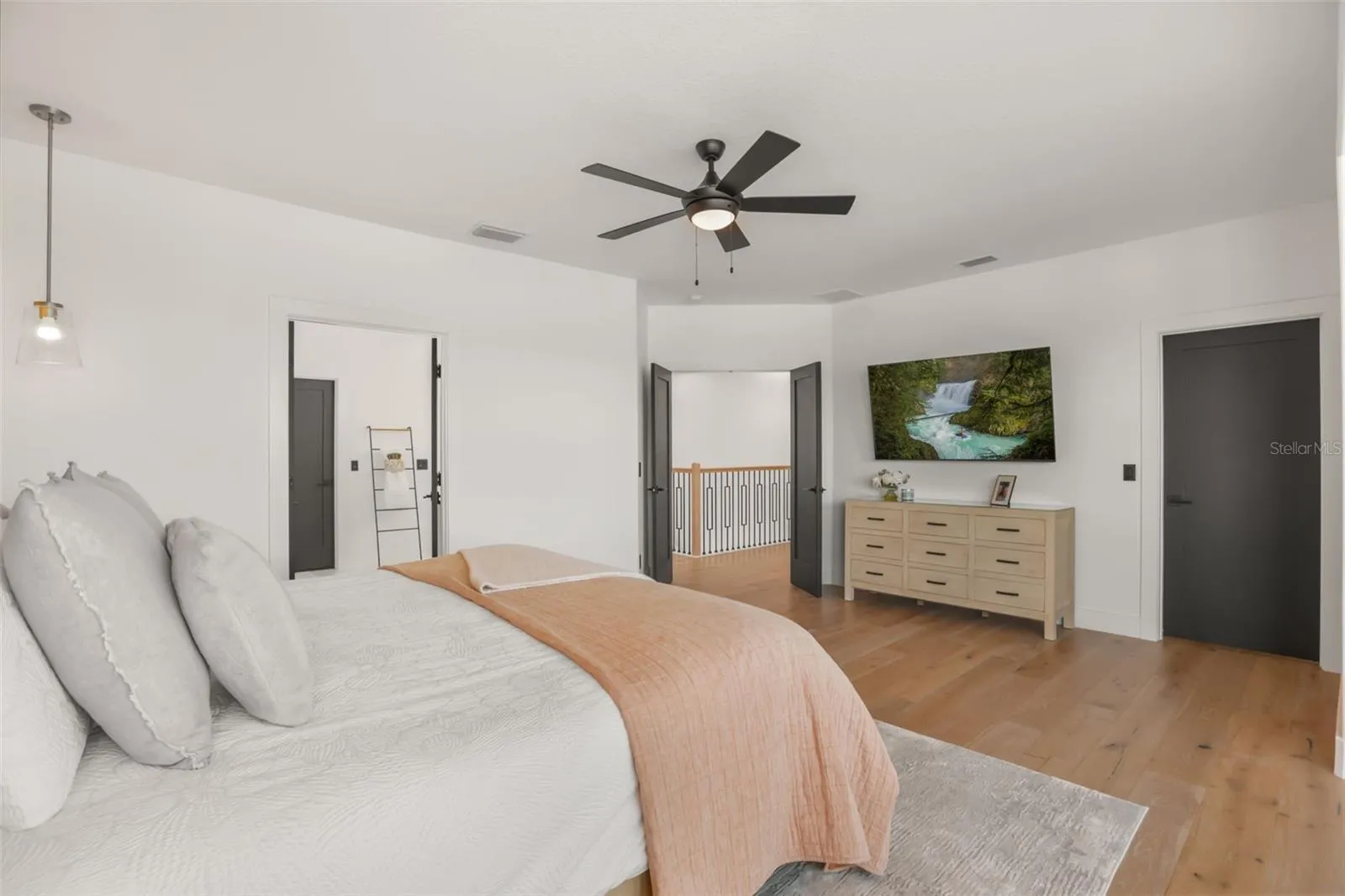 The primary suite offers an open, airy feel with wood flooring, neutral tones, and direct access to adjoining spaces.