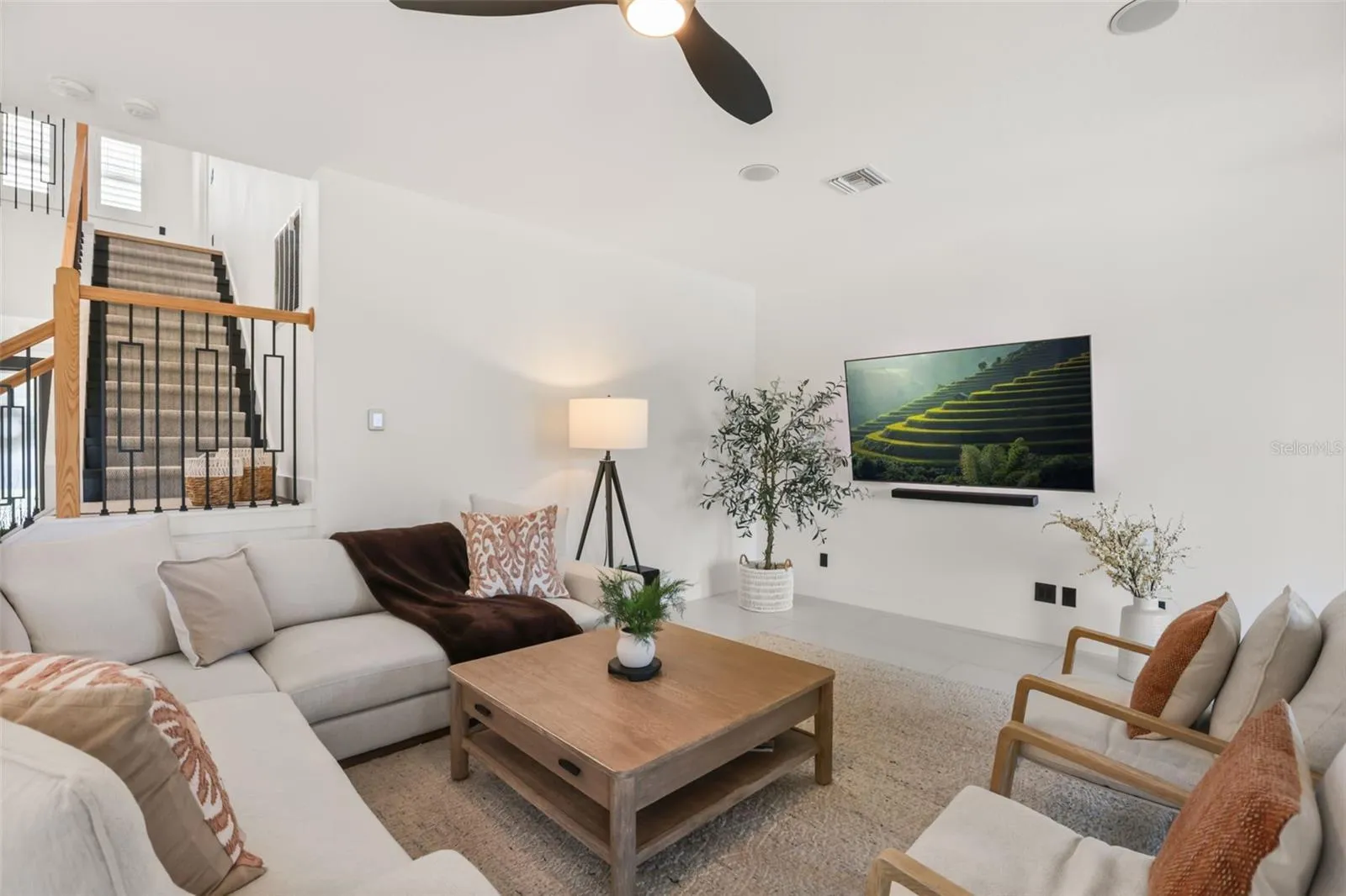 A comfortable gathering area with a wall-mounted TV, soft seating, and modern ceiling fan creates a relaxed everyday living space.
