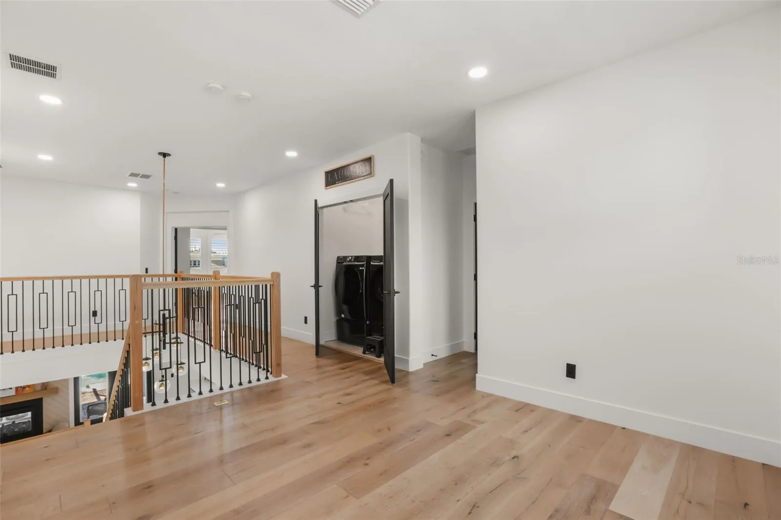 The upstairs landing features warm wood flooring, open railing details, recessed lighting, and convenient access to the laundry area.