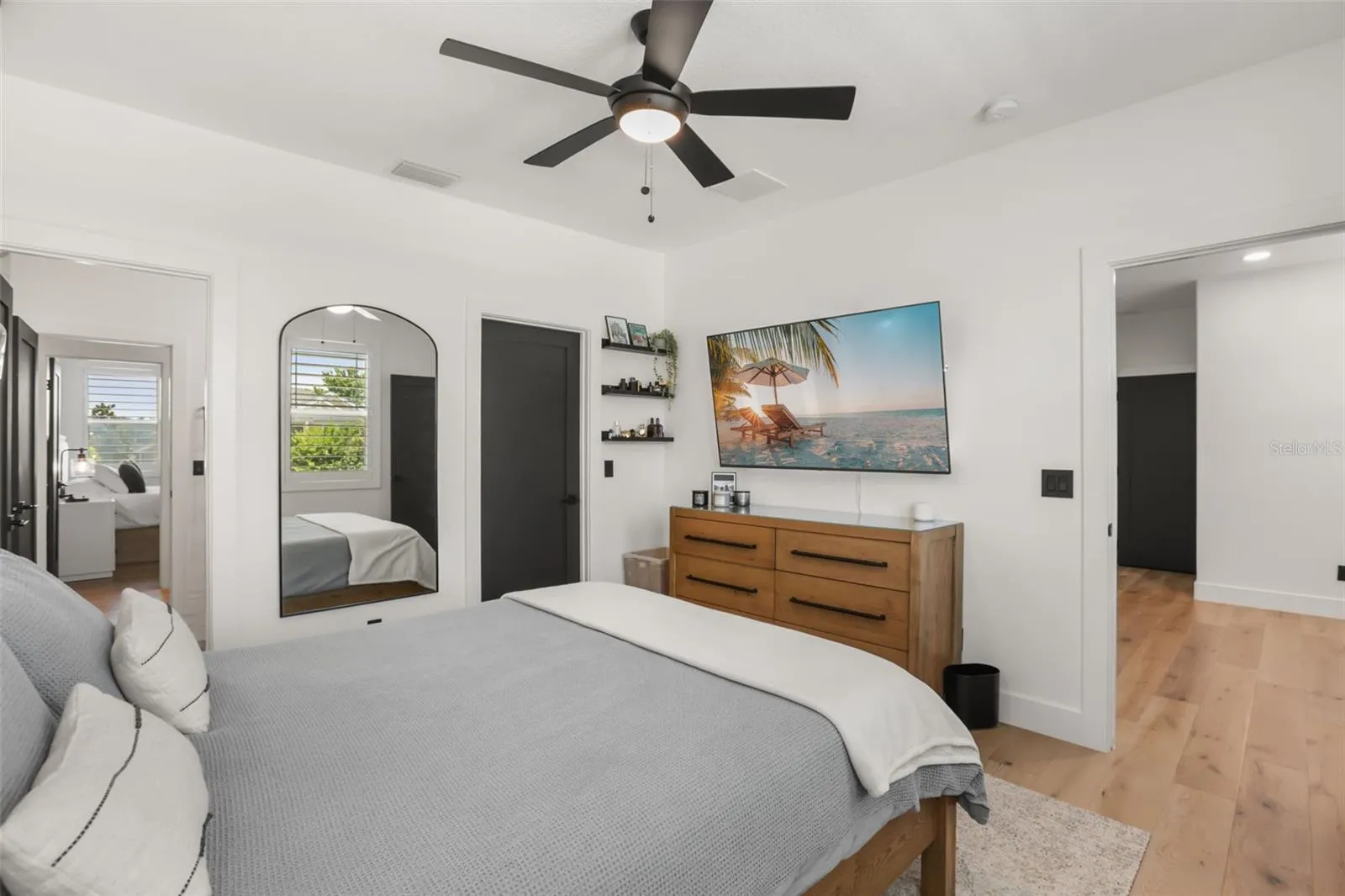 A well-sized bedroom features plantation shutters, wood flooring, a ceiling fan, and space for a dresser and media setup.