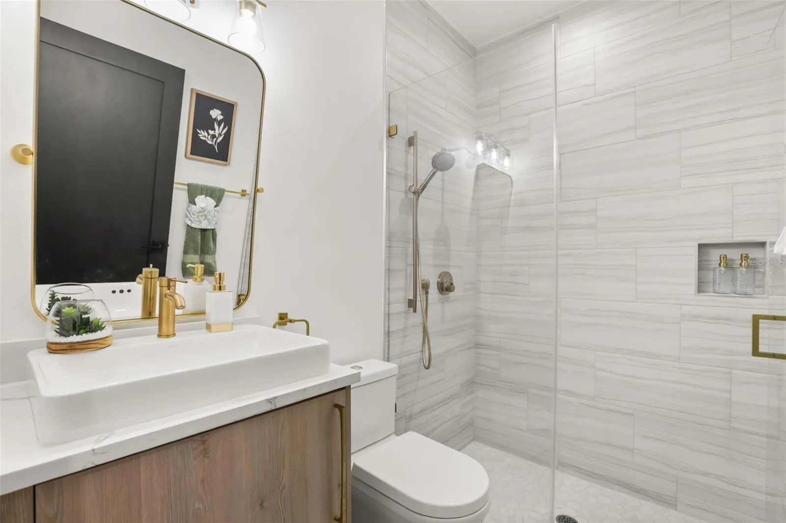 This stylish bath includes a walk-in shower with marble-look tile, brass accents, and a modern vanity with clean finishes.
