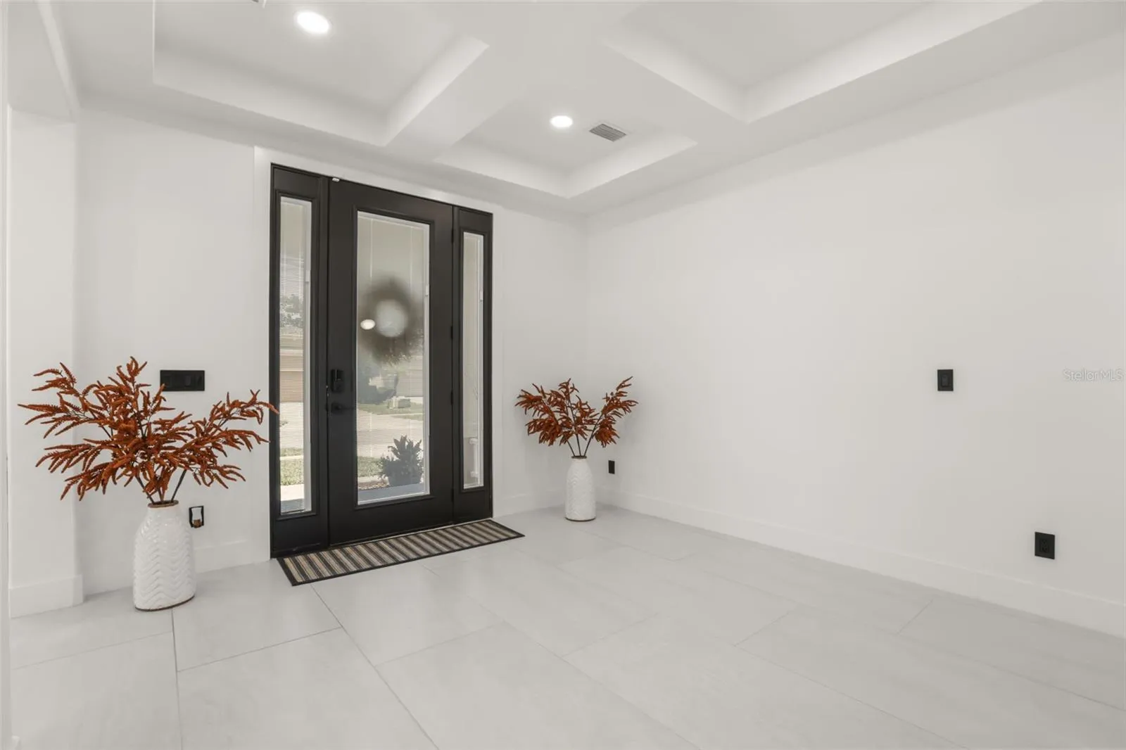 Black entry door with glass panels create a striking welcome, complemented by tray ceilings, recessed lighting, and neutral tile flooring.