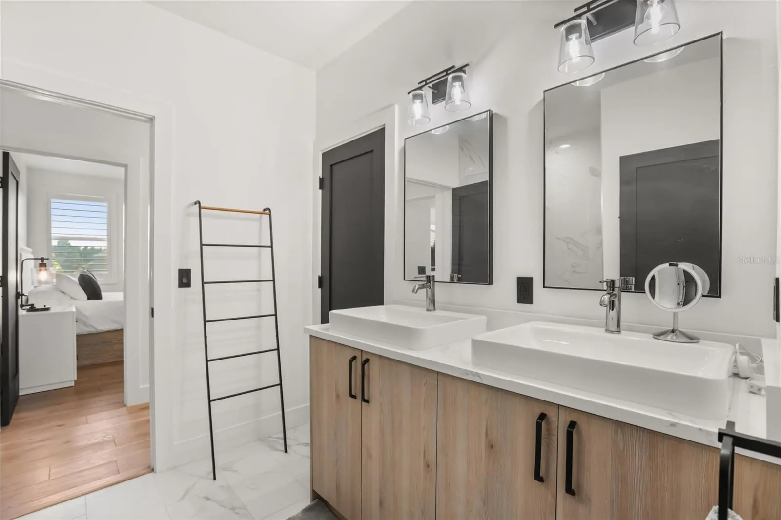 A closer view of the double vanity showcases clean lines, framed mirrors, and a bright connection to the adjoining bedroom.