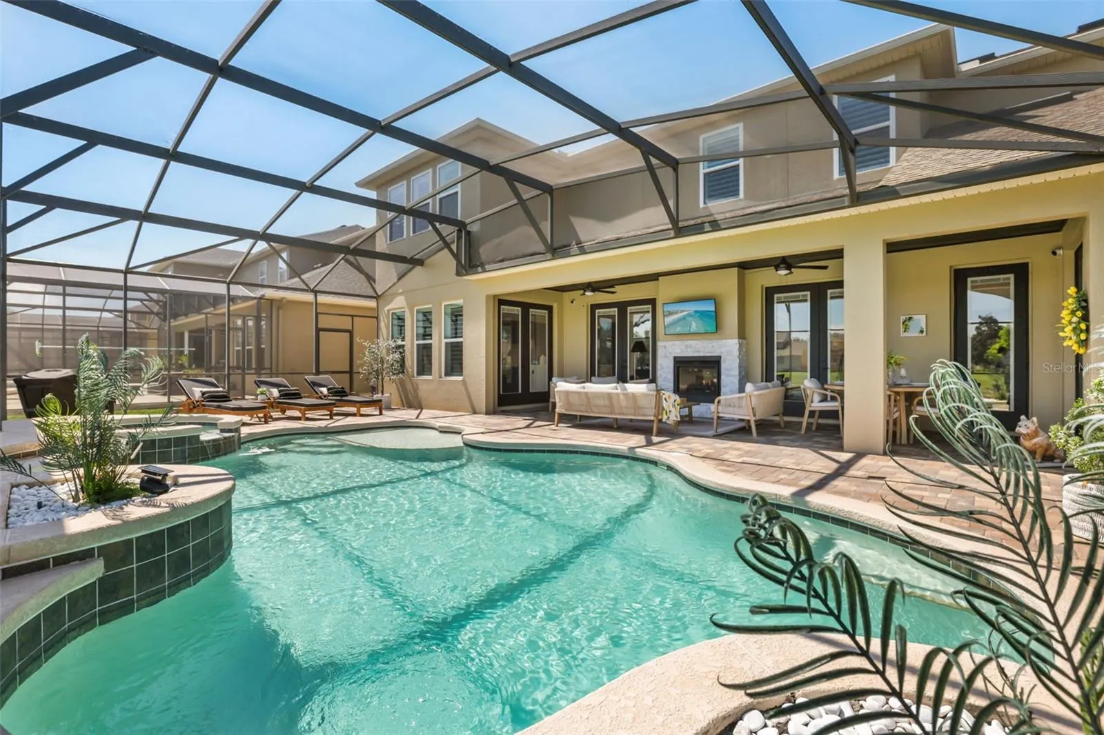 A wide rear view showcases the pool, spa, covered lanai, lounge seating, and easy access to the home’s outdoor living spaces.