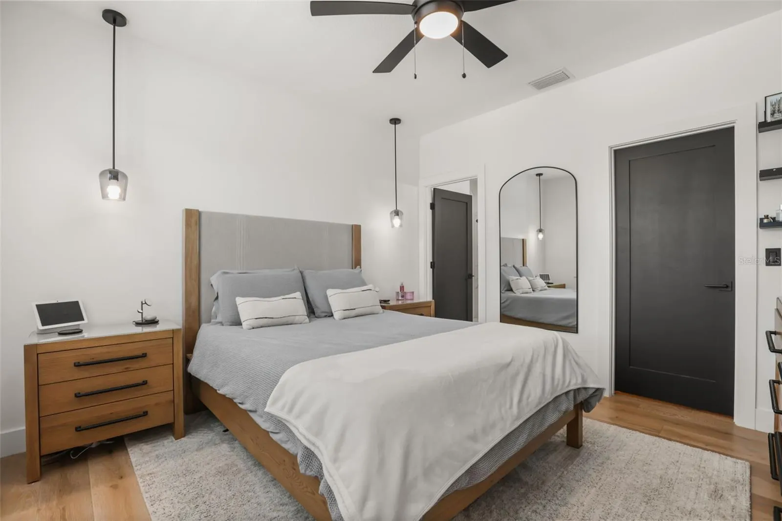 This bedroom offers wood flooring, pendant bedside lighting, a modern ceiling fan, and a clean neutral palette for flexible styling.
