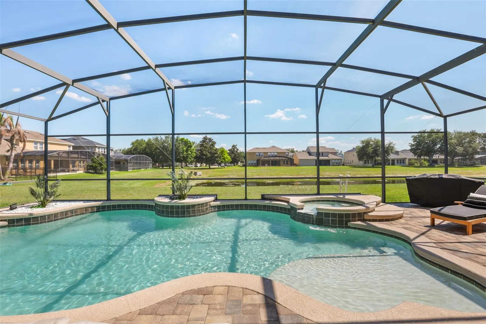 The screened pool area features a curved pool design, raised spa, shallow sun shelf, and open green views beyond the enclosure.