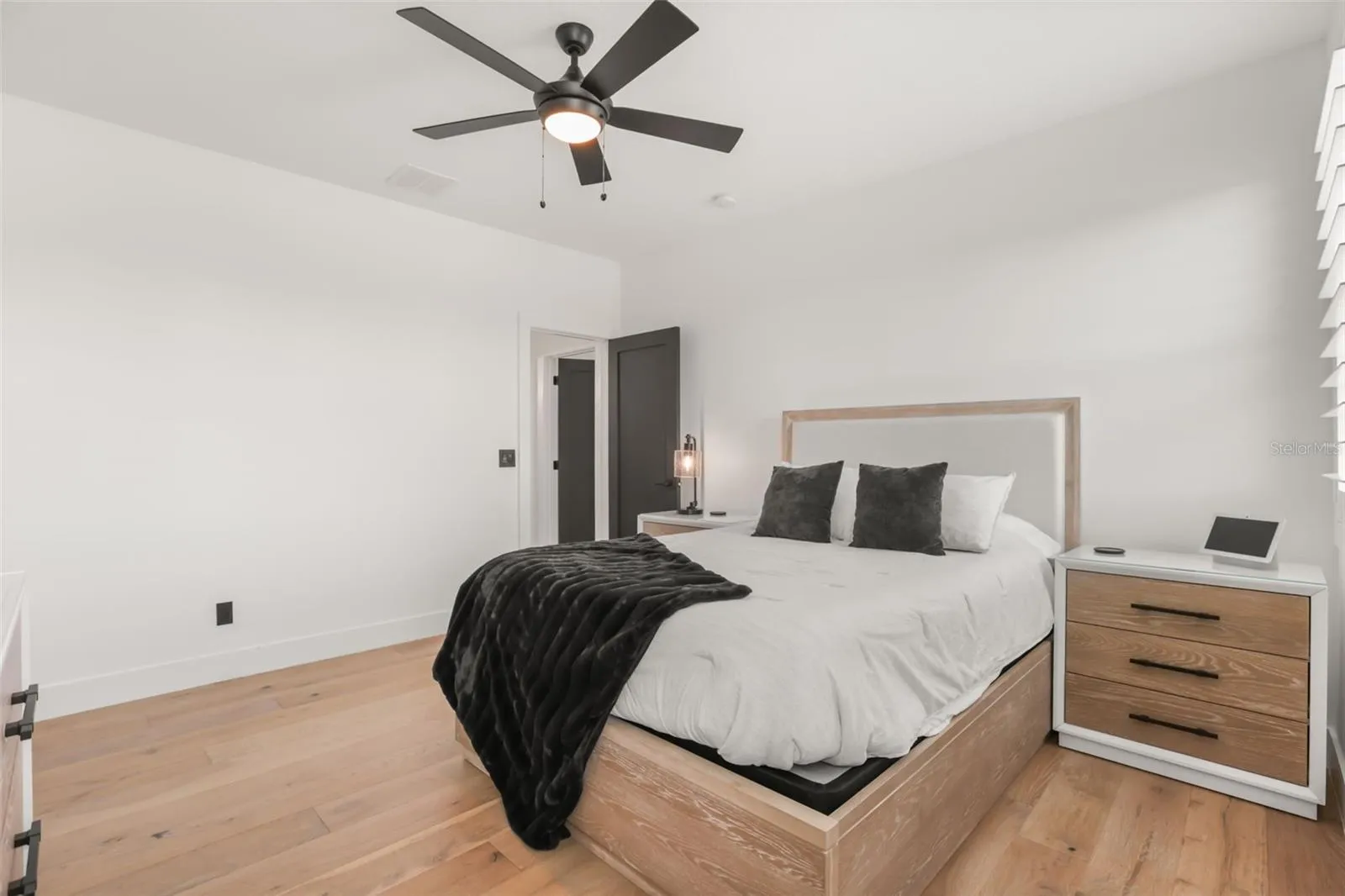 This bedroom features warm wood floors, a ceiling fan, neutral finishes, and a wood platform bed for a clean, modern feel.