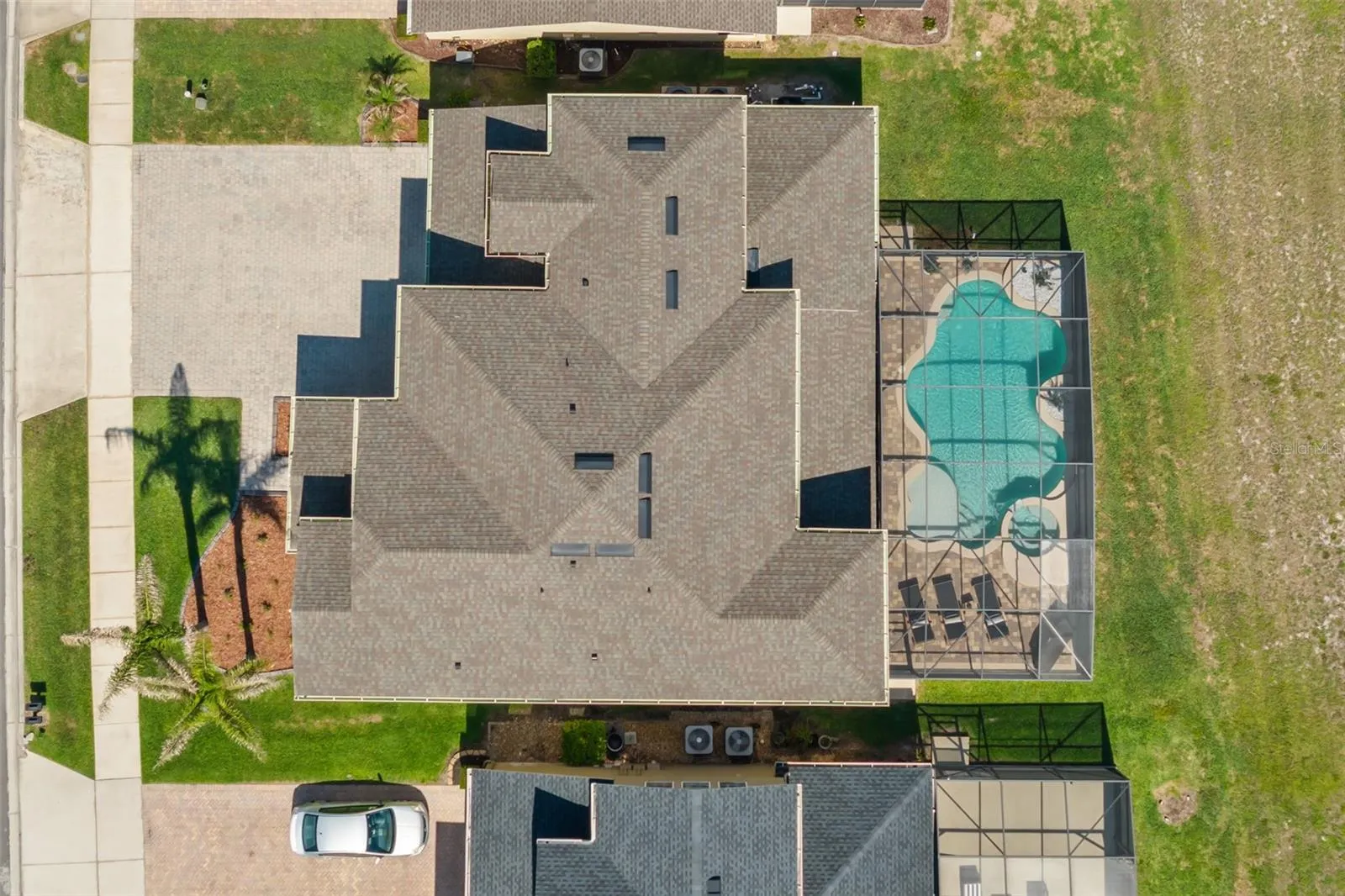 A top-down view captures the home’s roofline, paver driveway, screened pool area, and overall lot layout.