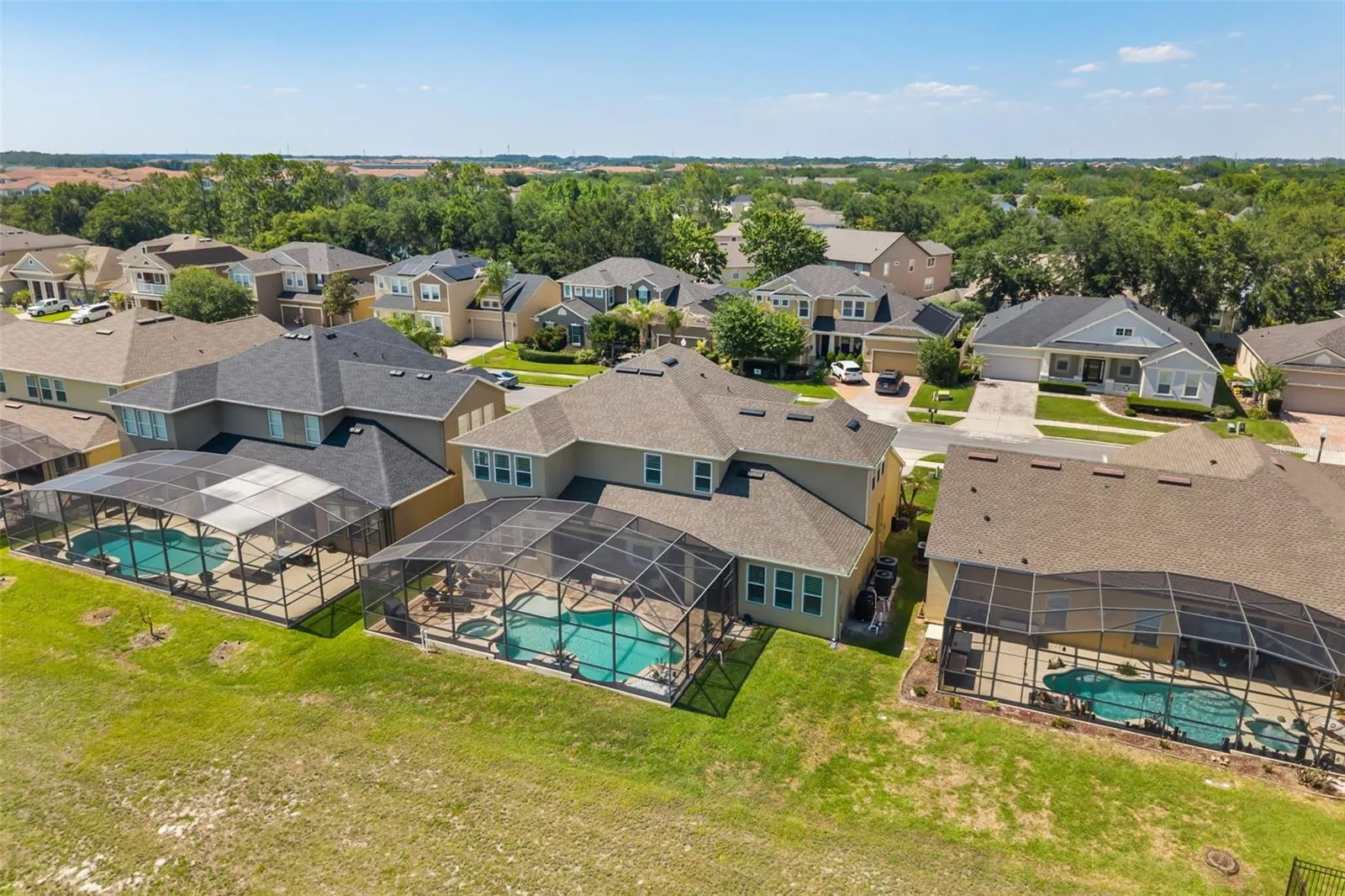 This aerial perspective highlights the screened pool enclosure, rear lawn, and surrounding neighborhood setting.