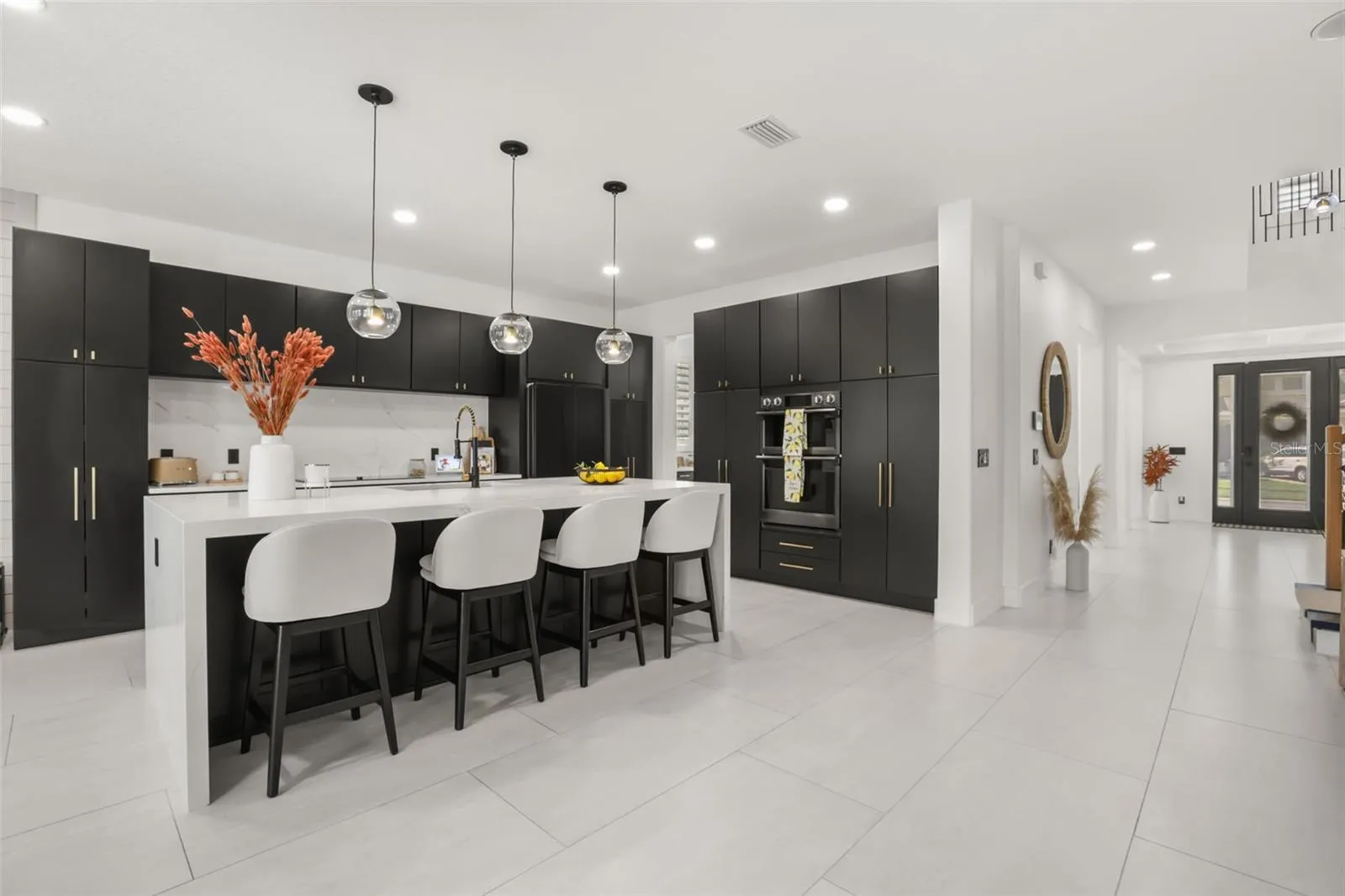 This wide kitchen view highlights the oversized island, built-in appliances, and open connection to the entry and surrounding living spaces.