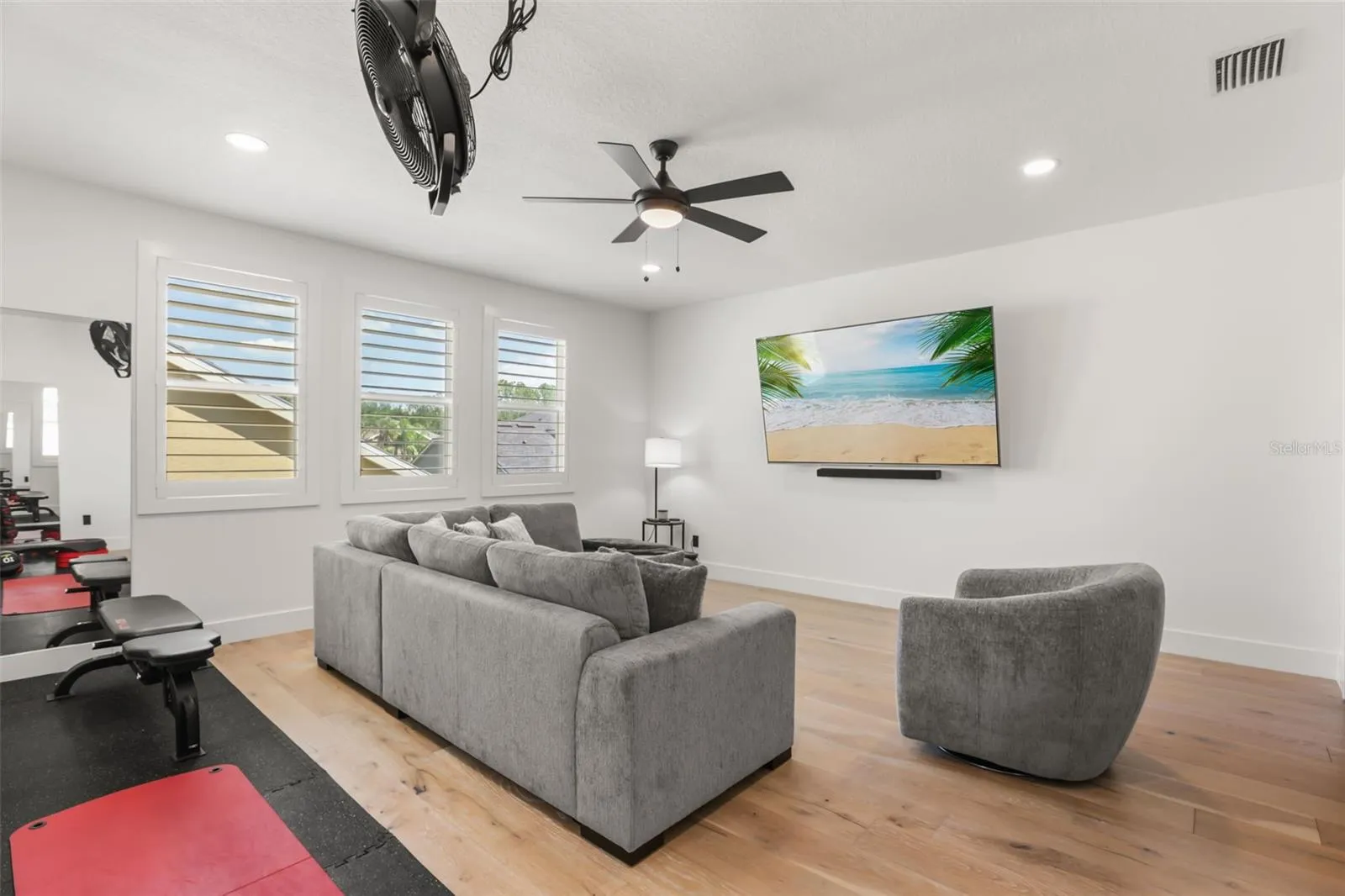 A comfortable sectional, wall-mounted TV, and nearby exercise area make this bonus room ideal for both relaxing and active use.