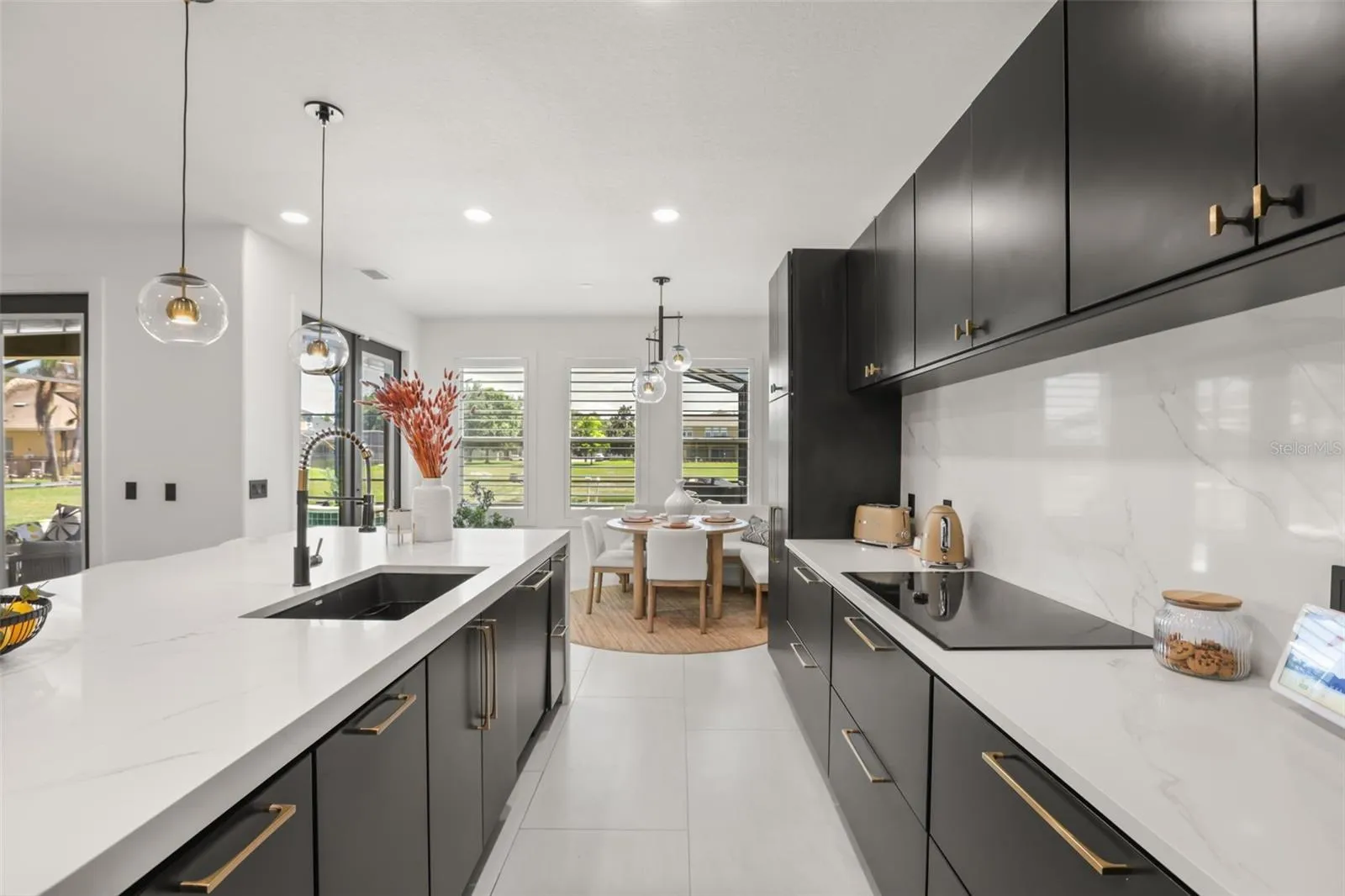 A bright kitchen corridor leads toward the breakfast nook, with plantation shutters, pendant lighting, and a spacious island enhancing the layout.