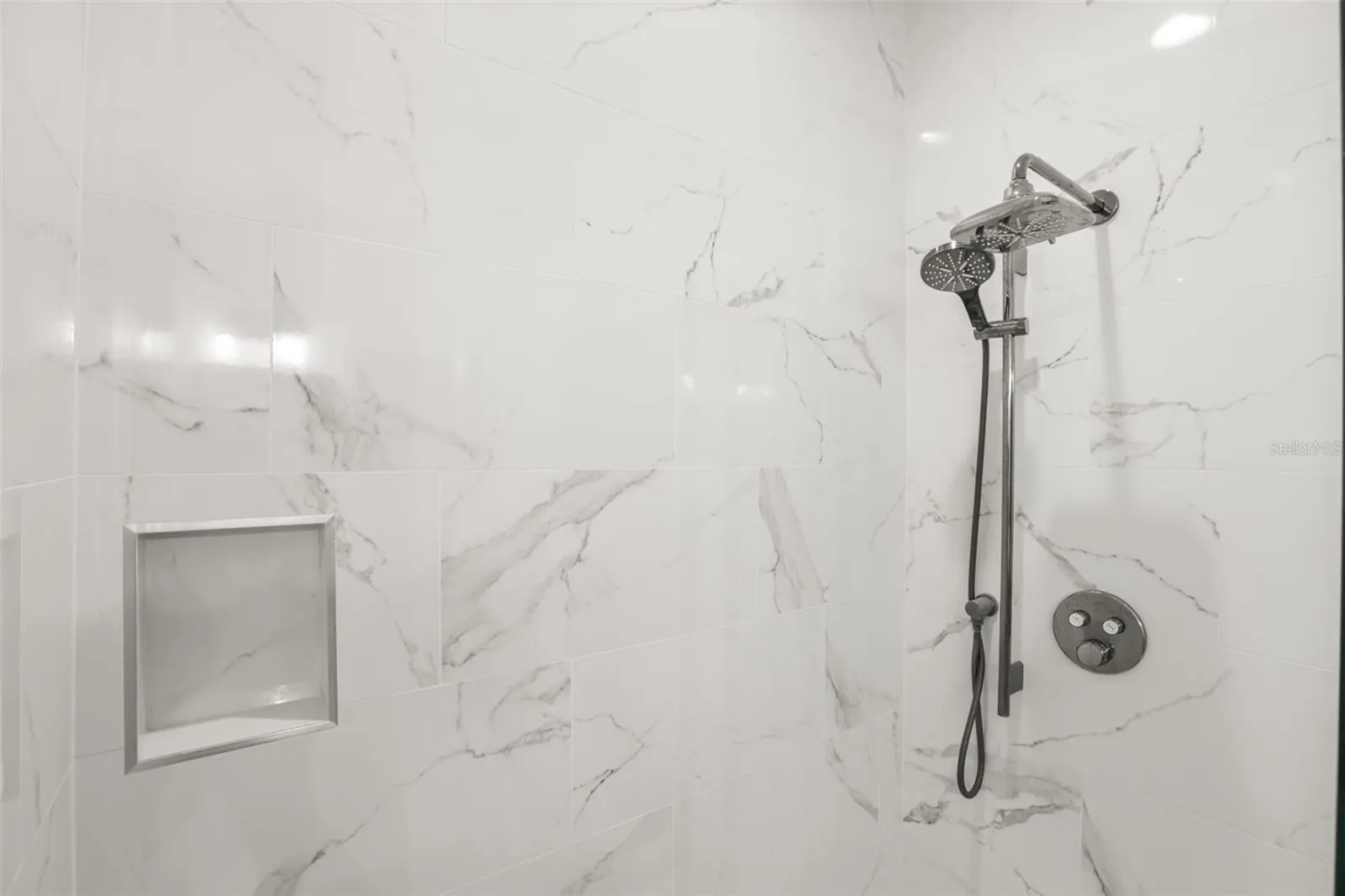 A detailed view highlights the marble-look tile surround, built-in niche, and upgraded shower fixture for a polished finish.