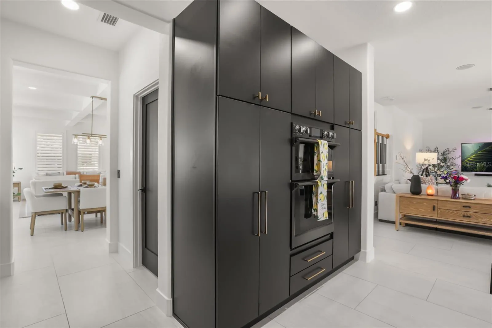 A wall of tall cabinetry with built-in double ovens provides generous storage and a clean, integrated look near the main living area.