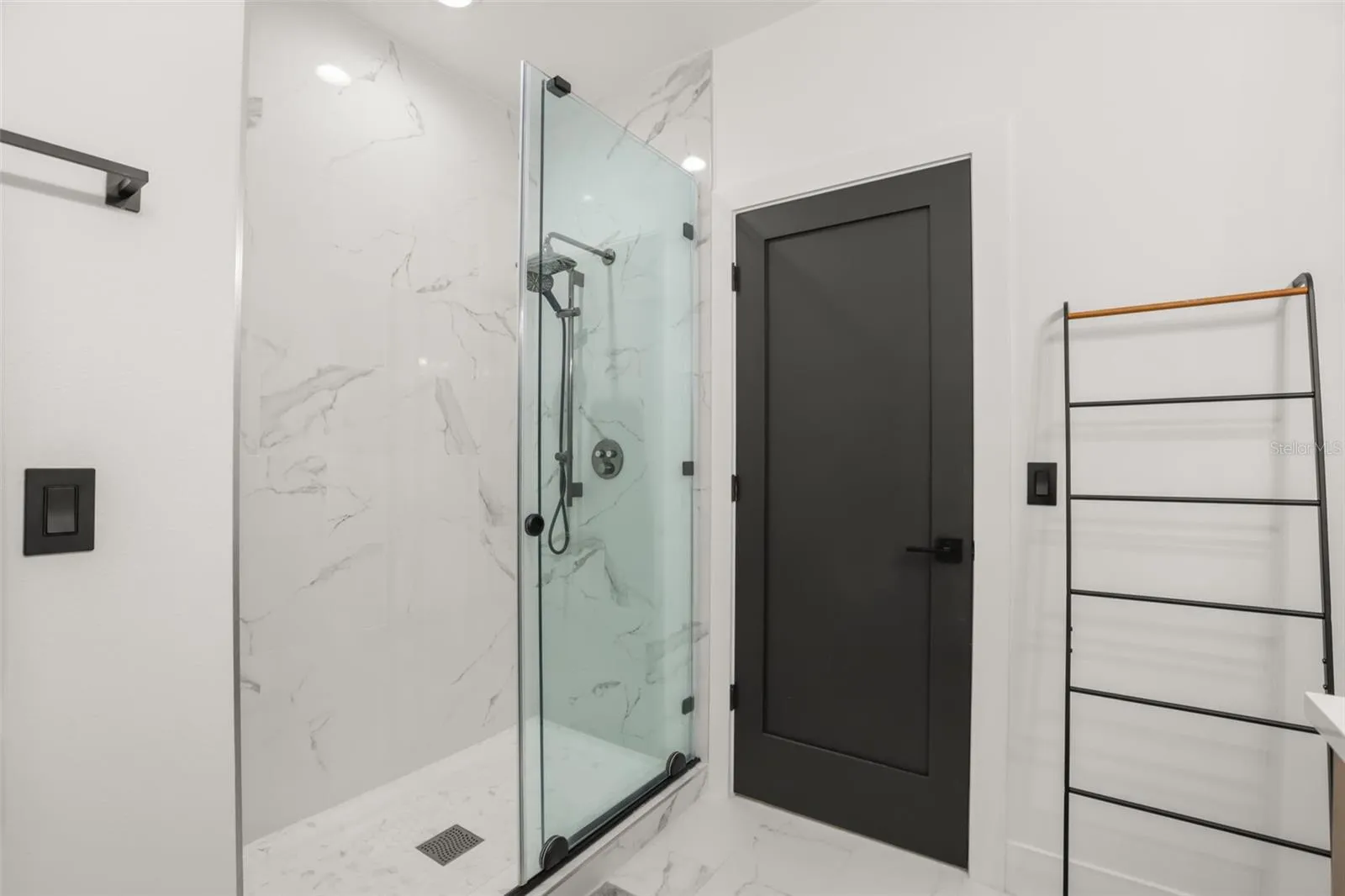 The glass-enclosed shower features marble-look tile, a built-in niche, black trim, and a sleek contemporary design.