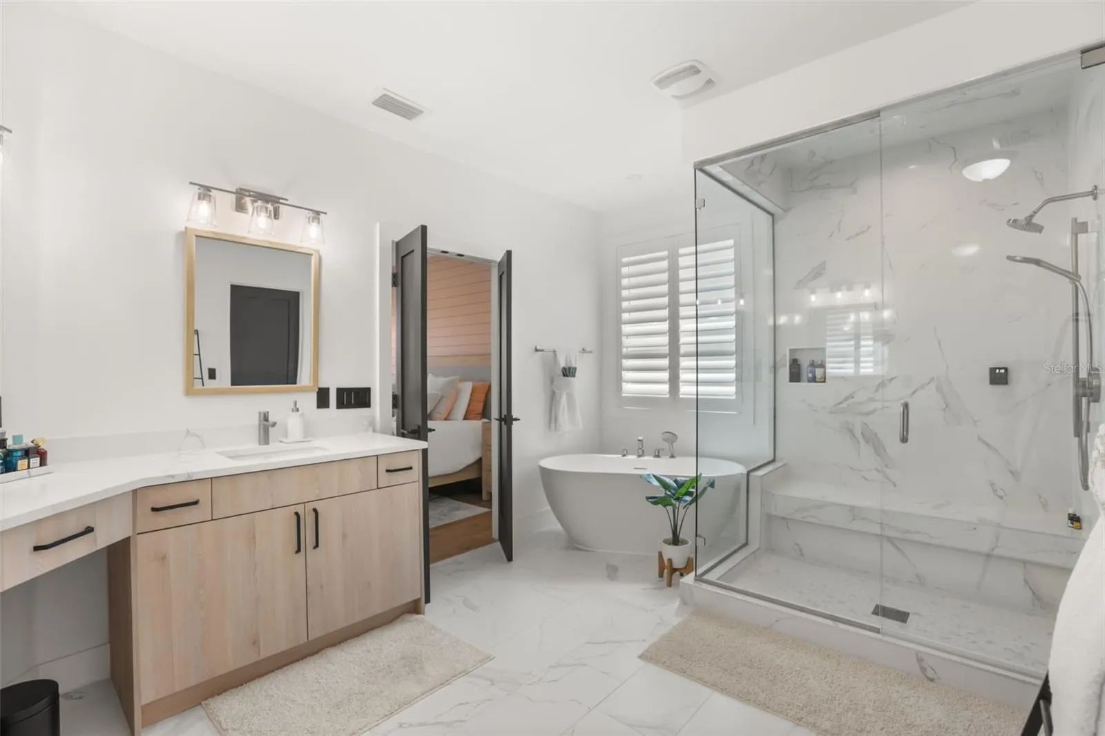 The primary bath features a freestanding soaking tub, glass-enclosed shower, dual vanity, and marble-look tile for a spa-inspired finish.