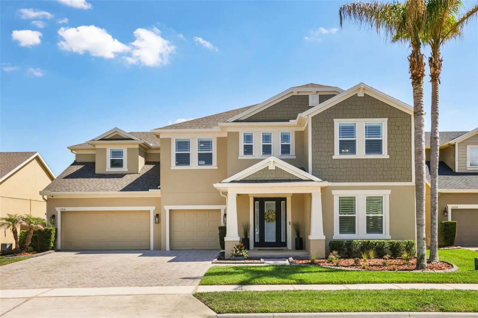 A polished two-story exterior with a paver driveway, three-car garage, covered entry, and manicured landscaping framed by mature palms.