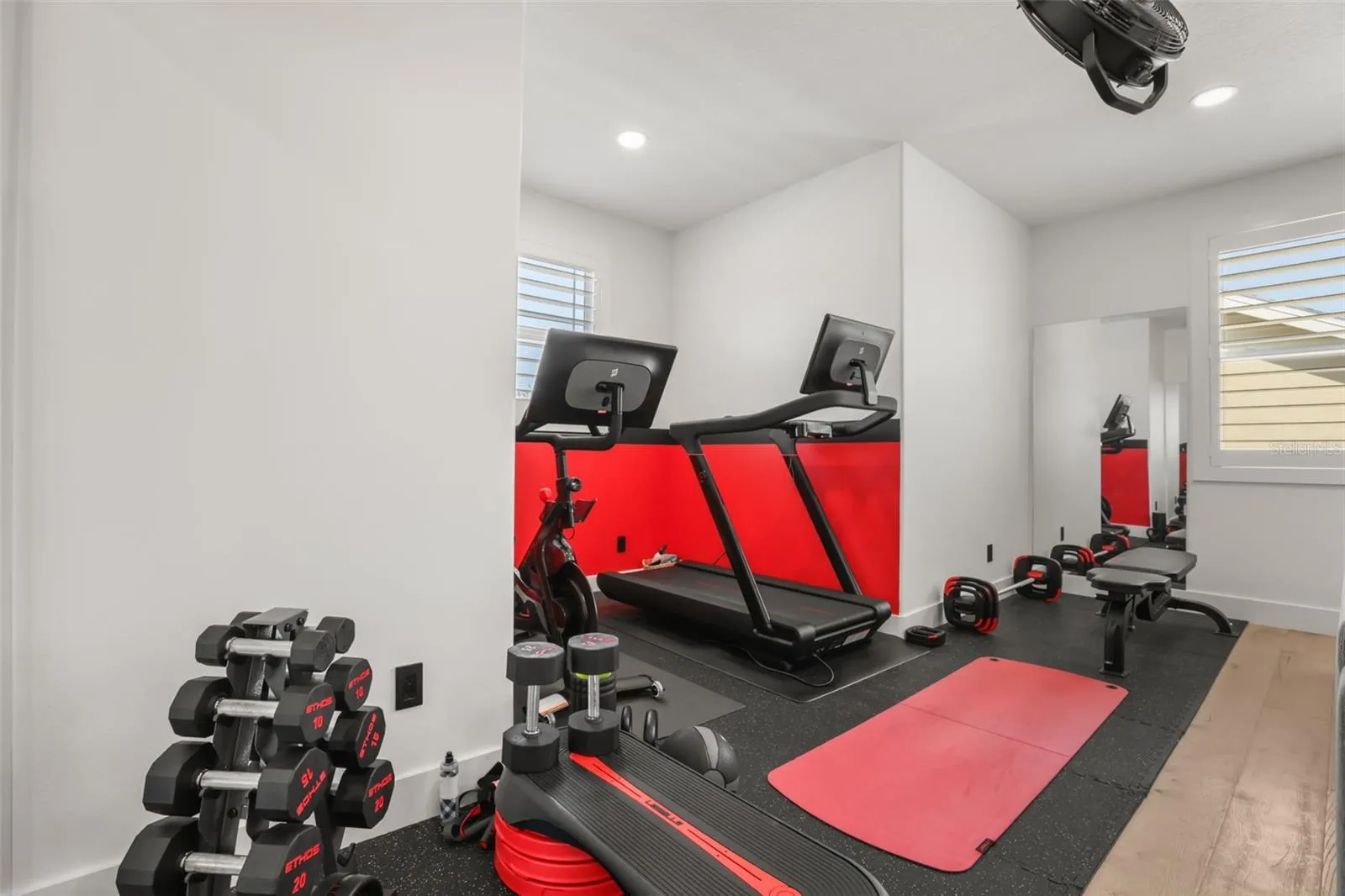 The fitness area includes rubber flooring, cardio equipment, dumbbell storage, and a bold accent wall for an energized workout setup.