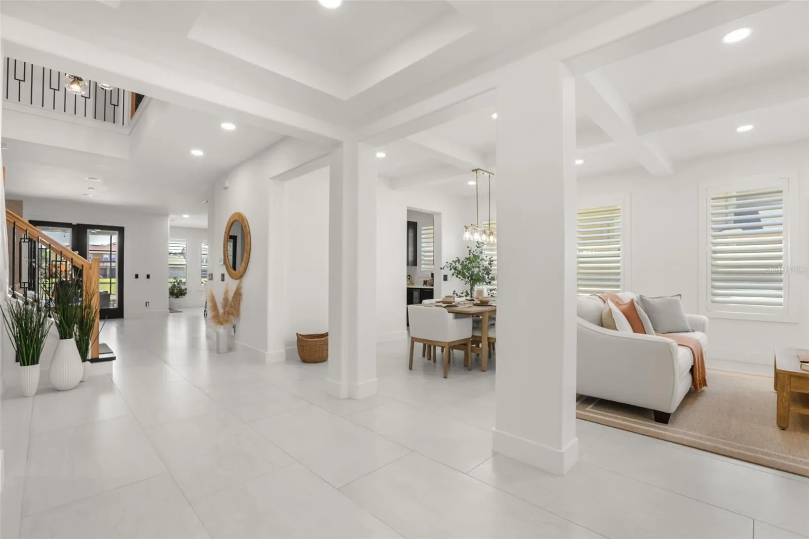 A bright entry opens to multiple living and dining spaces, featuring large-format tile flooring, tray ceilings, recessed lighting, and a clean modern palette.