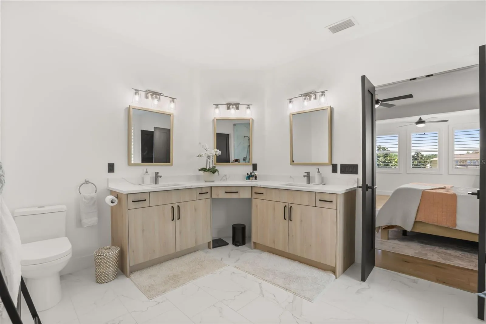 A spacious vanity layout with multiple sinks, light wood cabinetry, and framed mirrors offers both style and everyday function.