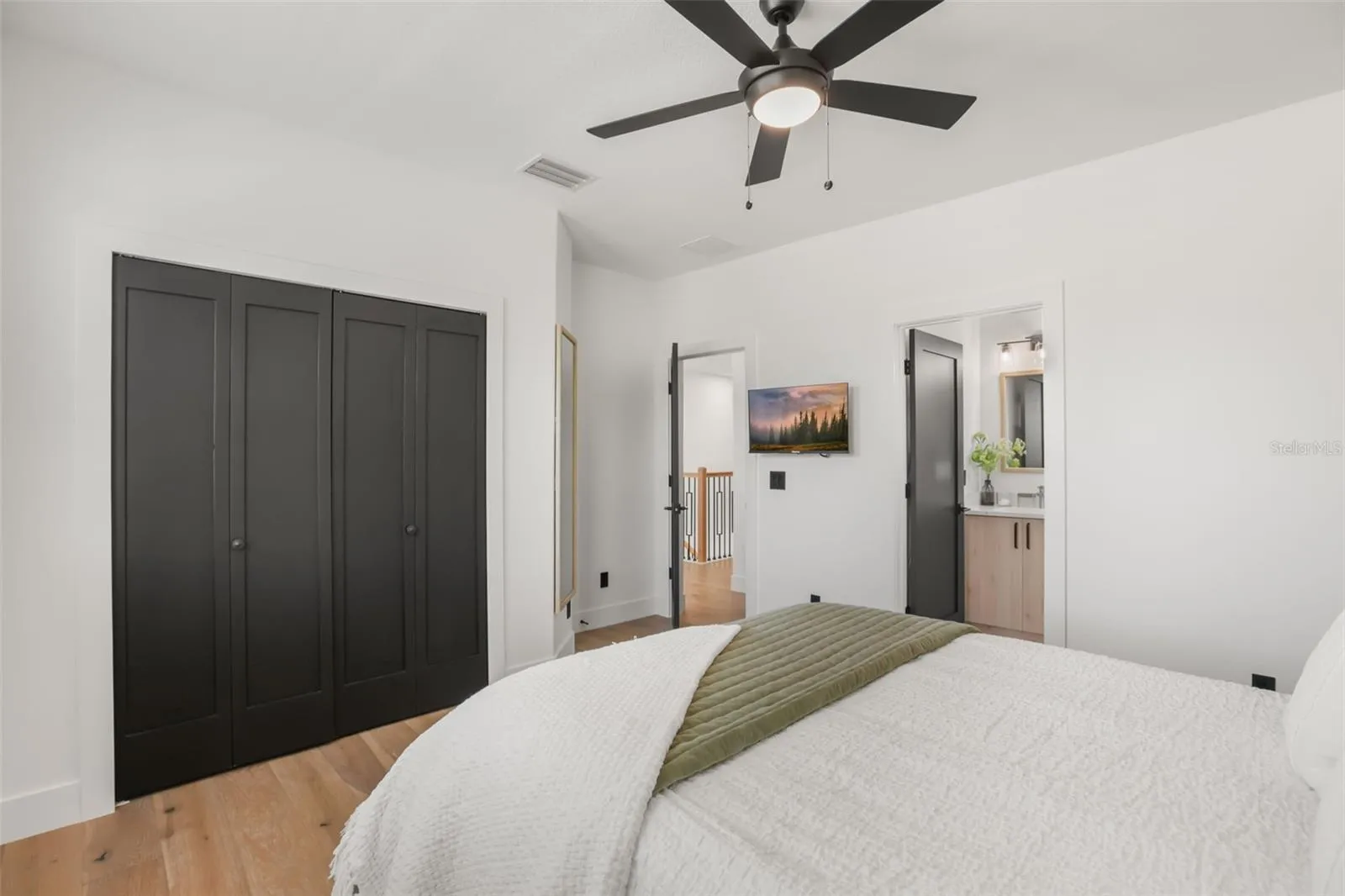 A bright bedroom view highlights dark closet doors, wood flooring, and convenient access to an adjoining bathroom.