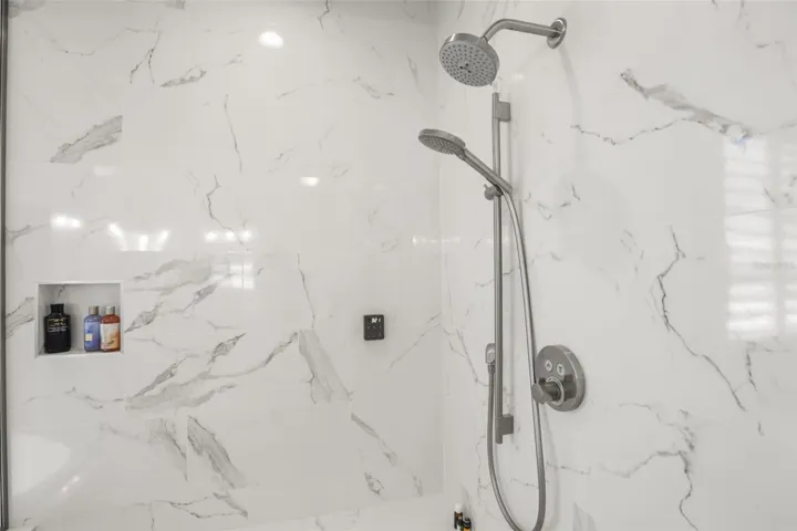 The oversized shower showcases marble-look tile, built-in niches, a bench, and multiple shower fixtures for an upgraded bathing experience.