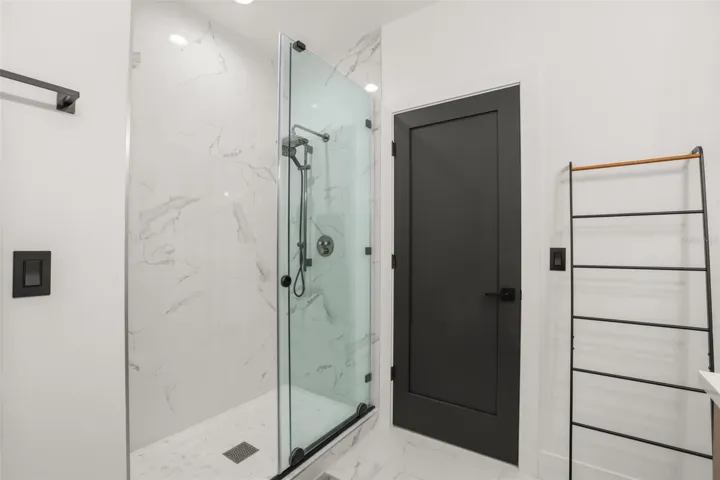 The glass-enclosed shower features marble-look tile, a built-in niche, black trim, and a sleek contemporary design.
