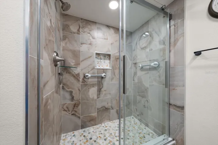 Guest bathroom featuring custom-designed tile work, removable safety grab bars, and a glass shower door.