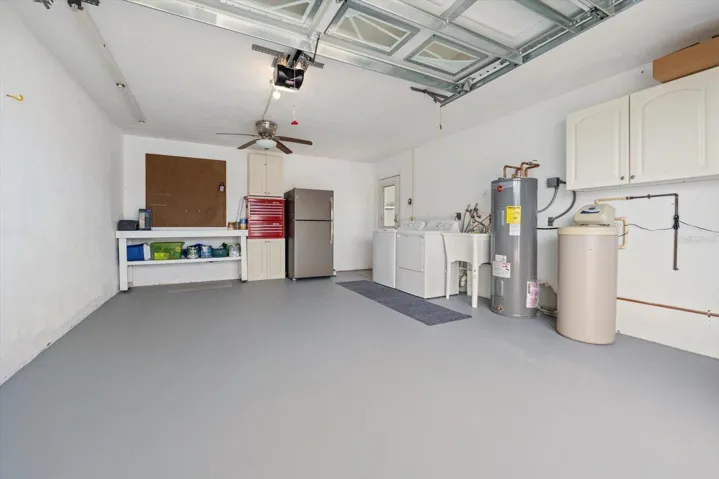 One-car garage featuring a laundry area with a sink, workbench, a garage refrigerator, a water softener system, and additional storage cabinetry.