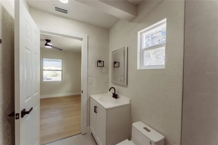 The brand new en suite bath features a white shaker vanity, matte black fixtures, and a framed mirror — with a natural light impact window and direct access to the primary bedroom.