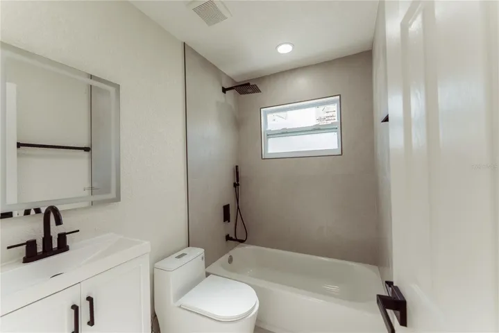 The fully updated second bathroom features a tiled tub/shower combo with a rainfall showerhead, matte black fixtures, white shaker vanity, and a natural light impact window — all brand new.