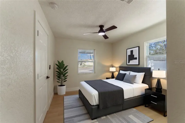 Two new impact windows flood the primary bedroom with natural light, while warm luxury vinyl flooring and a modern ceiling fan complete the space. The en suite bathroom is just steps away through the private door. (Virtually Staged.)