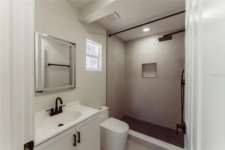 No detail was spared in this fully updated en suite, showcasing a floor-to-ceiling tiled walk-in shower with a built-in niche, rainfall showerhead, matte black hardware, and dark hex tile flooring for a sleek, modern finish.
