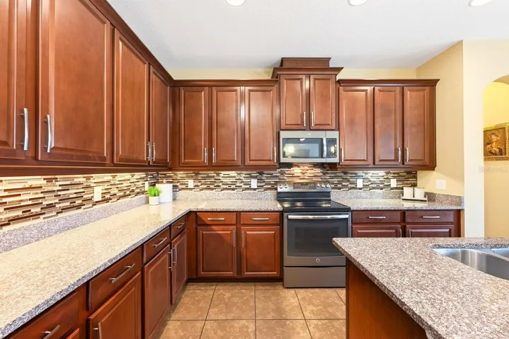 Featuring 42-inch cabinetry, stone countertops, a stylish tile backsplash, STAINLESS STEEL APPLIANCES, a large center island with breakfast bar seating, a closet pantry, and an adjoining Breakfast Nook with PEACEFUL VIEWS of the pool area, this Kitchen is sure to impress.