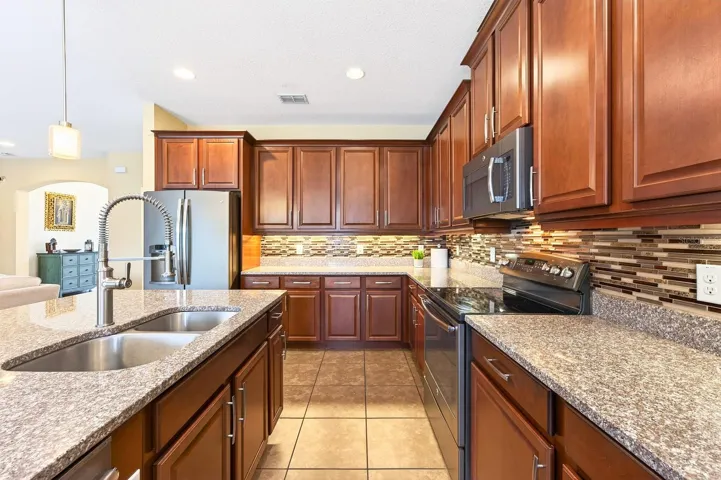 Featuring 42-inch cabinetry, stone countertops, a stylish tile backsplash, STAINLESS STEEL APPLIANCES, a large center island with breakfast bar seating, a closet pantry, and an adjoining Breakfast Nook with PEACEFUL VIEWS of the pool area, this Kitchen is sure to impress.
