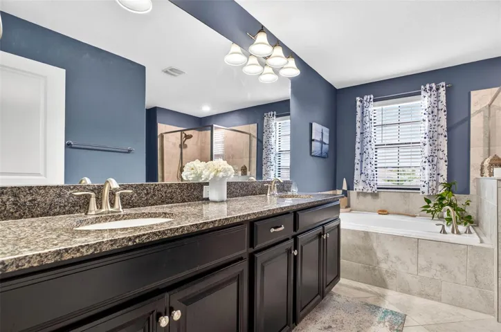 Primary bathroom with dual vanities, garden tub, walk in shower and blinds