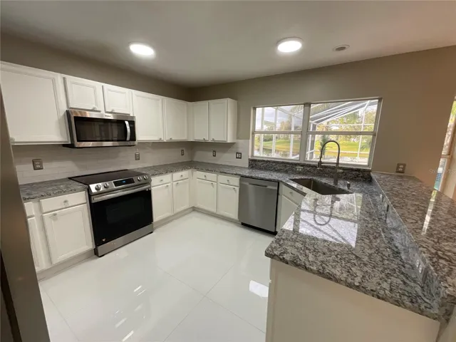 Kitchen featuring granite counters, stainless steel appliances, sea stone door pulls and a farmhouse sink.