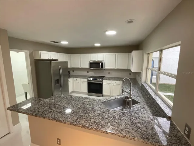 Kitchen featuring granite counters, stainless steel appliances, sea stone door pulls and a farmhouse sink.