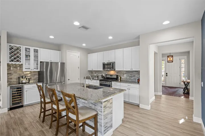 Kitchen with upgraded cabinetry, granite countertops, stainless steel appliances, tile backsplash, and wine fridge