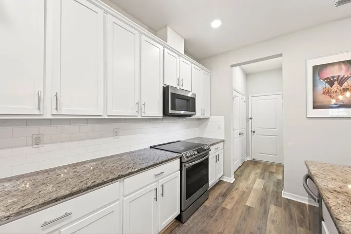 The BEAUTIFULLY APPOINTED KITCHEN presents granite countertops, mostly new stainless steel appliances, subway tile backsplash, a closet pantry, abundant cabinetry, and a large center island with BREAKFAST BAR SEATING that serves as the heart of the home.