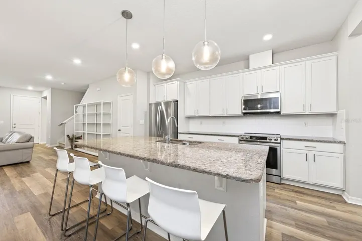 The BEAUTIFULLY APPOINTED KITCHEN presents granite countertops, mostly new stainless steel appliances, subway tile backsplash, a closet pantry, abundant cabinetry, and a large center island with BREAKFAST BAR SEATING that serves as the heart of the home.