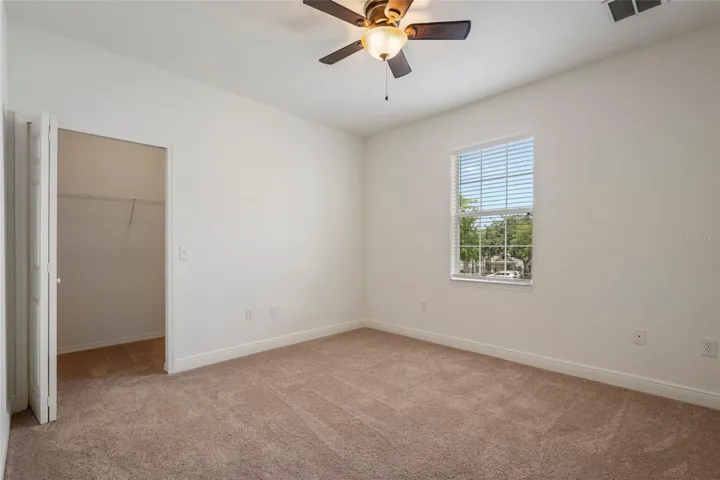 Primary bedroom from opposite view as you enter room, large walk in closet on far wall,  ceiling fan and blinds on window with large window for natural light.