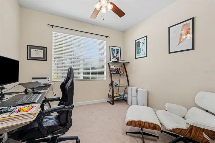 Second bedroom/junior suite via pocket door access, currently used as home office with desk, ceiling fan, natural light in Tampa FL 33647