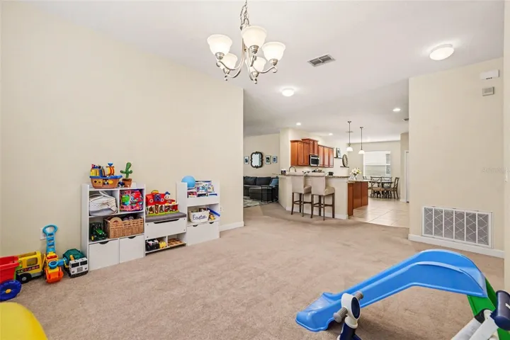 Open flex bonus space showing full depth, chandelier, and direct sightline through to kitchen, bar seating, and dining area in Tampa FL 33647. Foyer to the far right (not visible)