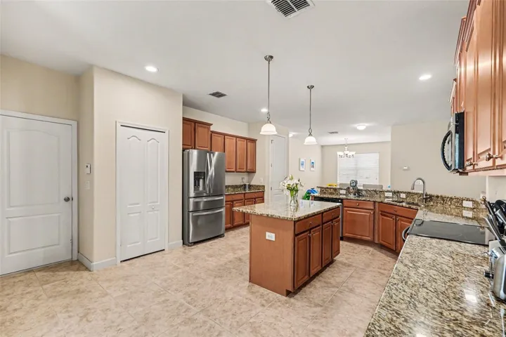 Kitchen with wood cabinetry, granite counters, center island, full-size pantry door, door to 3 car garage, and stainless French door refrigerator in Tampa FL 33647