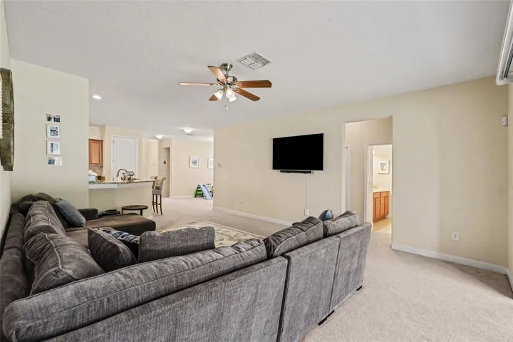 Large family room showing full open floor plan depth, ceiling fan, natural light, and open connection to kitchen in Tampa FL 33647. Entry to 2 bedrooms and double sink full bathroom to the far right.