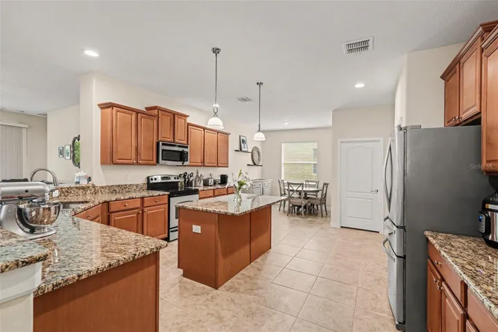 Large kitchen with granite island, full stainless appliance suite, pendant lights, and open view to breakfast nook and dining area in Tampa FL 33647. Laundry room door visible. Pantry and garage to the far right (not visible)
