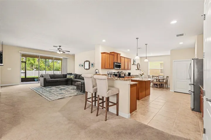 Wide-angle view of open-concept kitchen, family room, and granite bar seating area with stainless appliances and sliding glass door to screened lanai in Tampa FL 33647