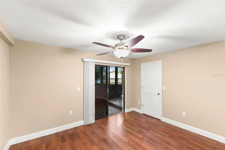 Spacious second bedroom featuring wood-look flooring, a ceiling fan, walk-in closet, and access to the screened lanai.