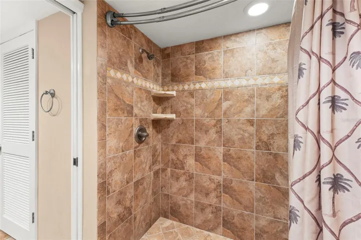 The tiled walk-in shower features floor-to-ceiling tile, decorative accent detailing, and built-in corner shelving.